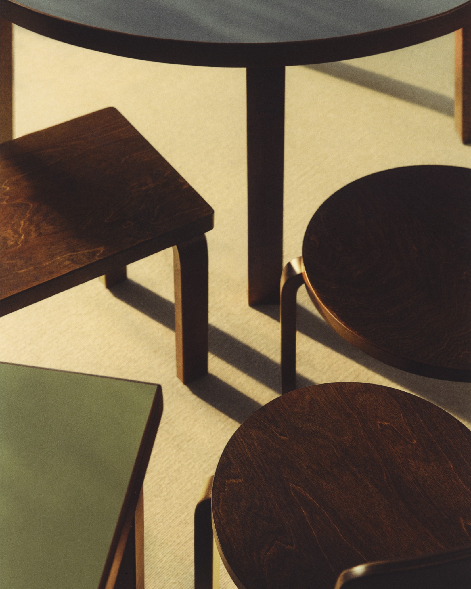 Detail of Artek wooden stools and a table in directional sunlight