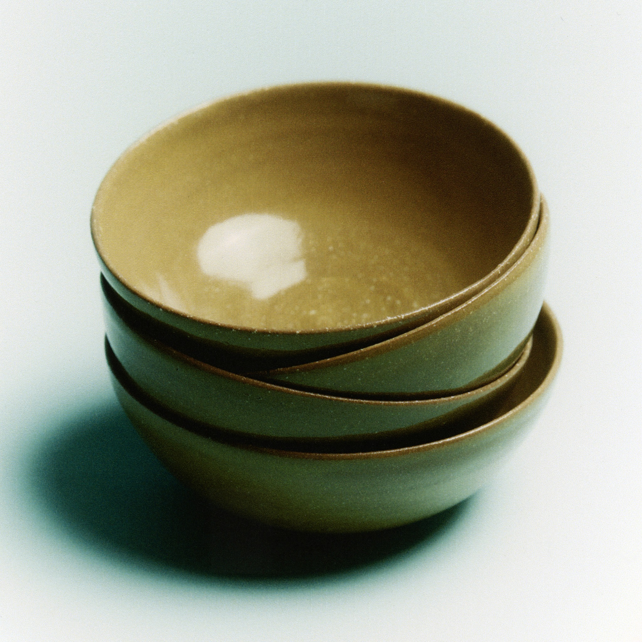 Stacked green ceramic bowls on a pale studio surface
