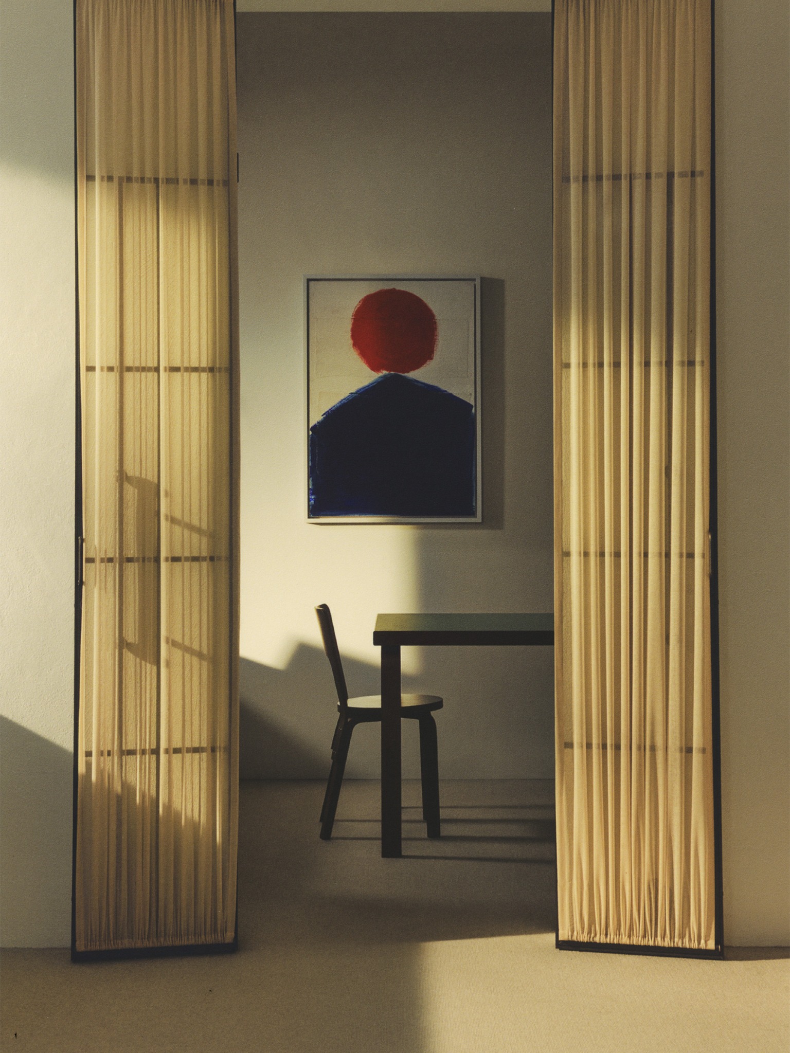 Sunlit Artek interior viewed through a doorway with an artwork and stool
