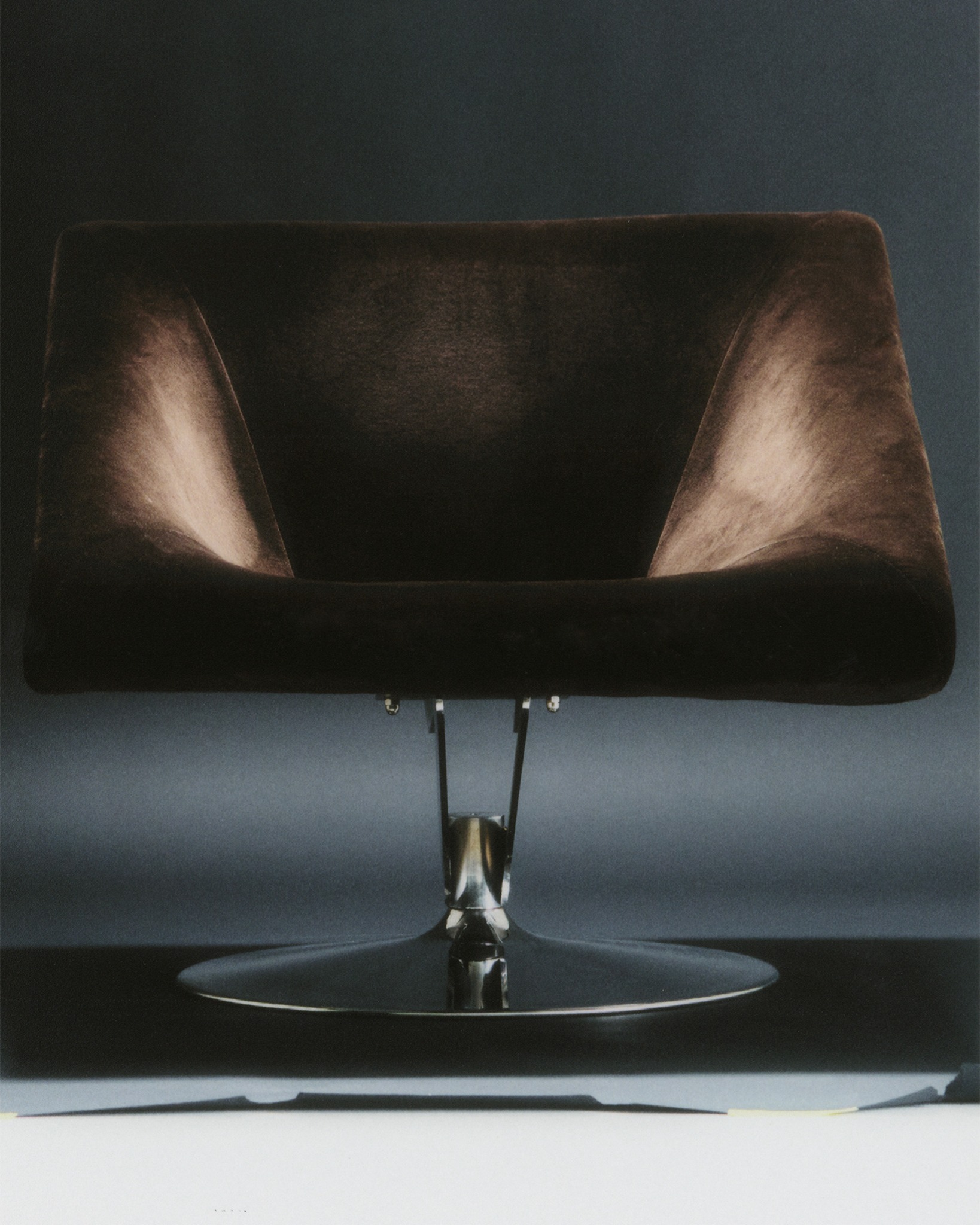 Brown upholstered swivel chair photographed against a dark backdrop