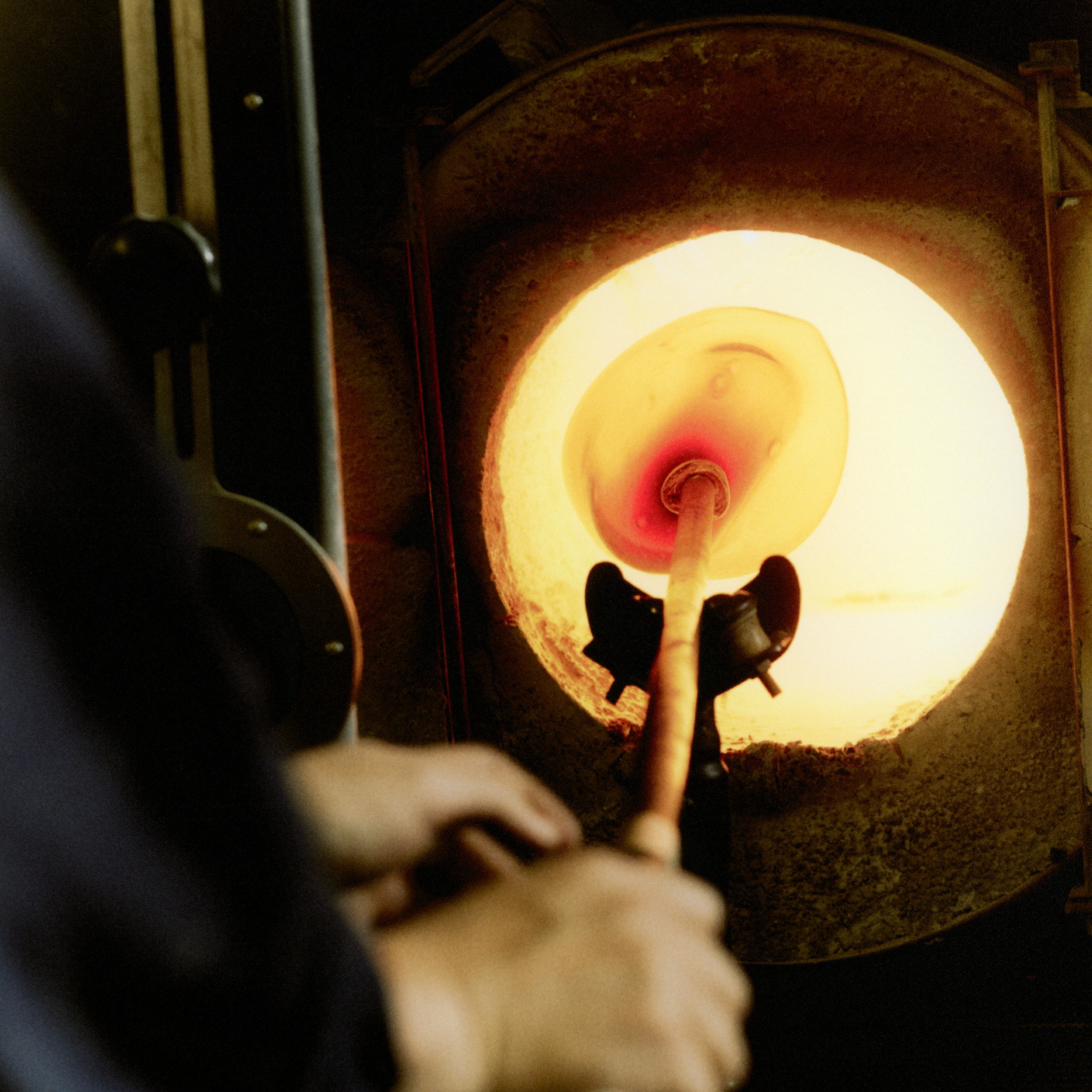 Glass being heated on a blowpipe inside a glowing workshop furnace