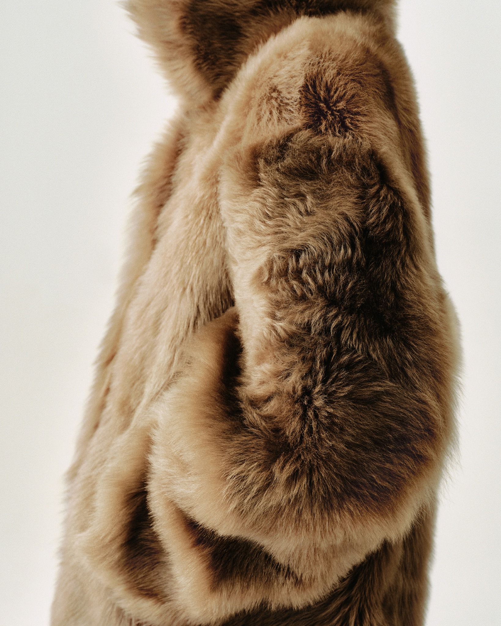 Close-up of a textured brown and cream Filippa K fur coat against a pale studio background