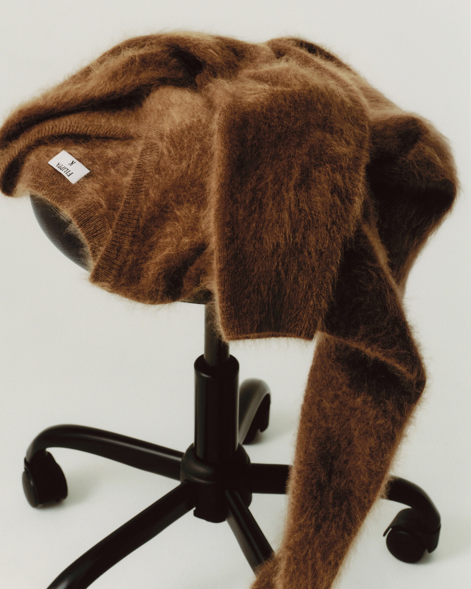 Brown Filippa K knitted sweater draped over a black studio stool