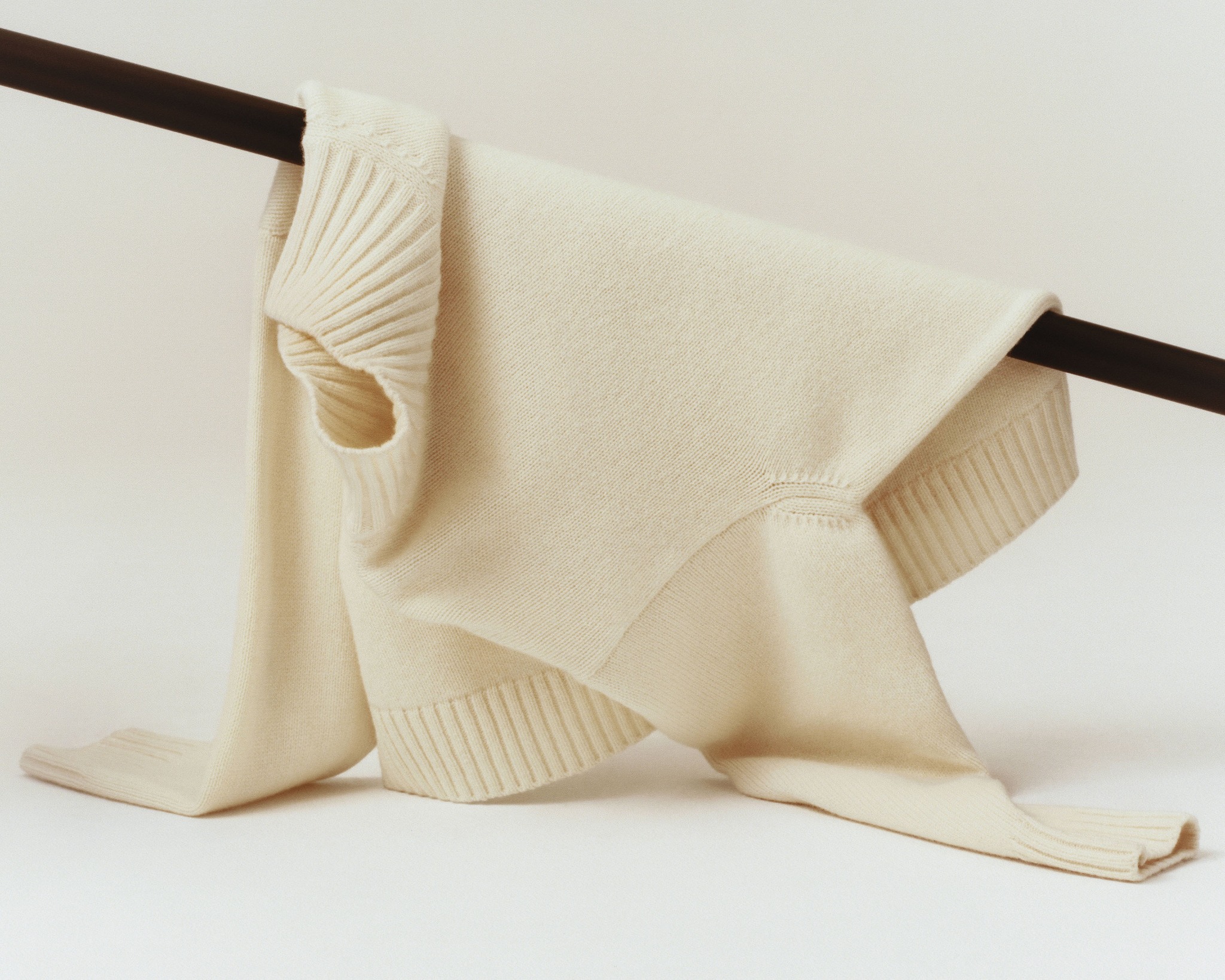 White Filippa K knitted sweater draped over a dark rail against a pale studio background